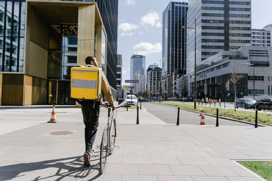 Entregador de bicicleta com bolsa térmica atravessando a cidade