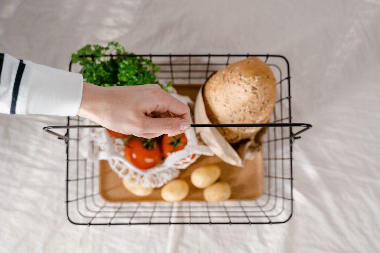 Mão segurando cesta com pão, batatas, tomates e verduras