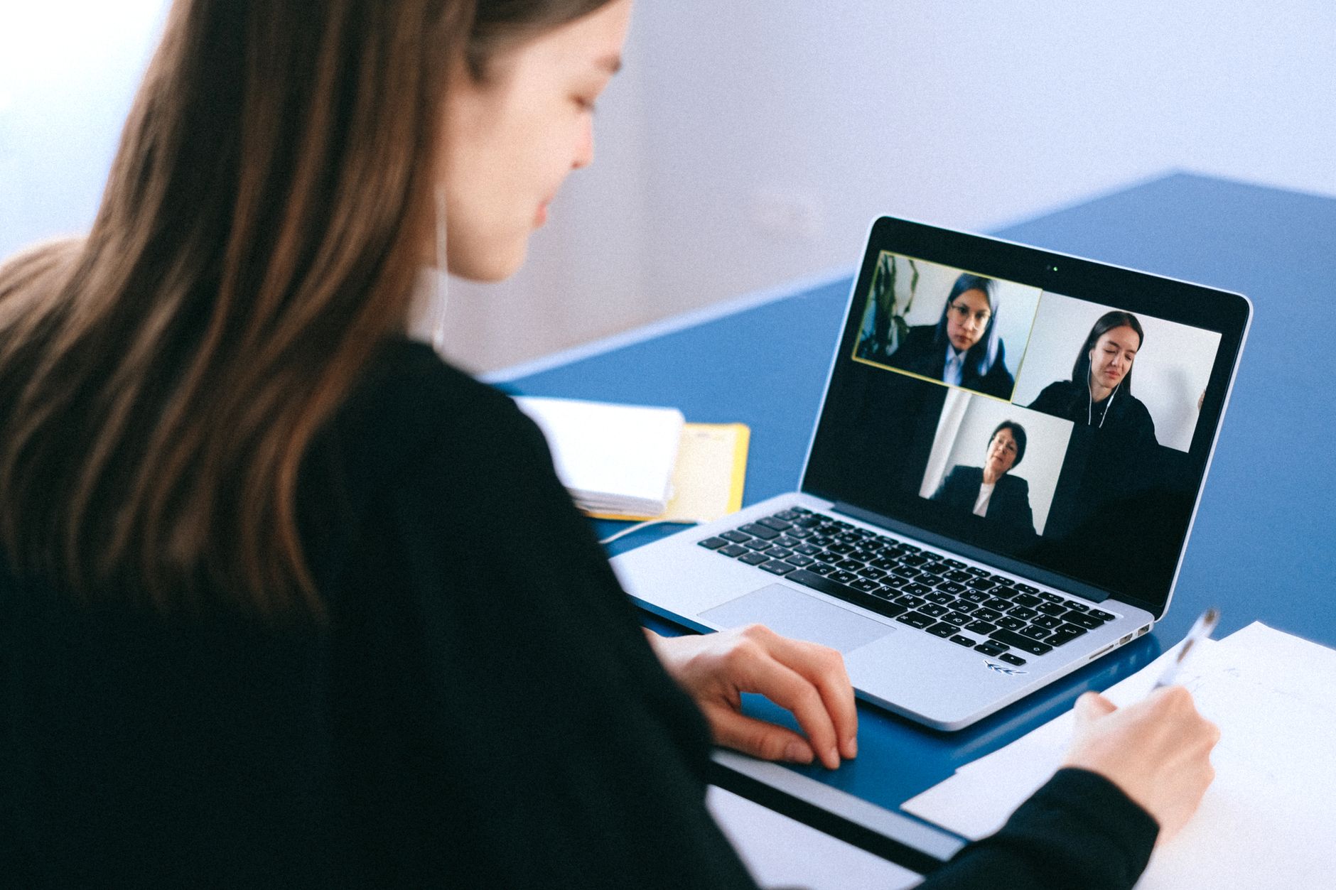 Mulher participando de videoconferência em notebook e fazendo anotações em casa