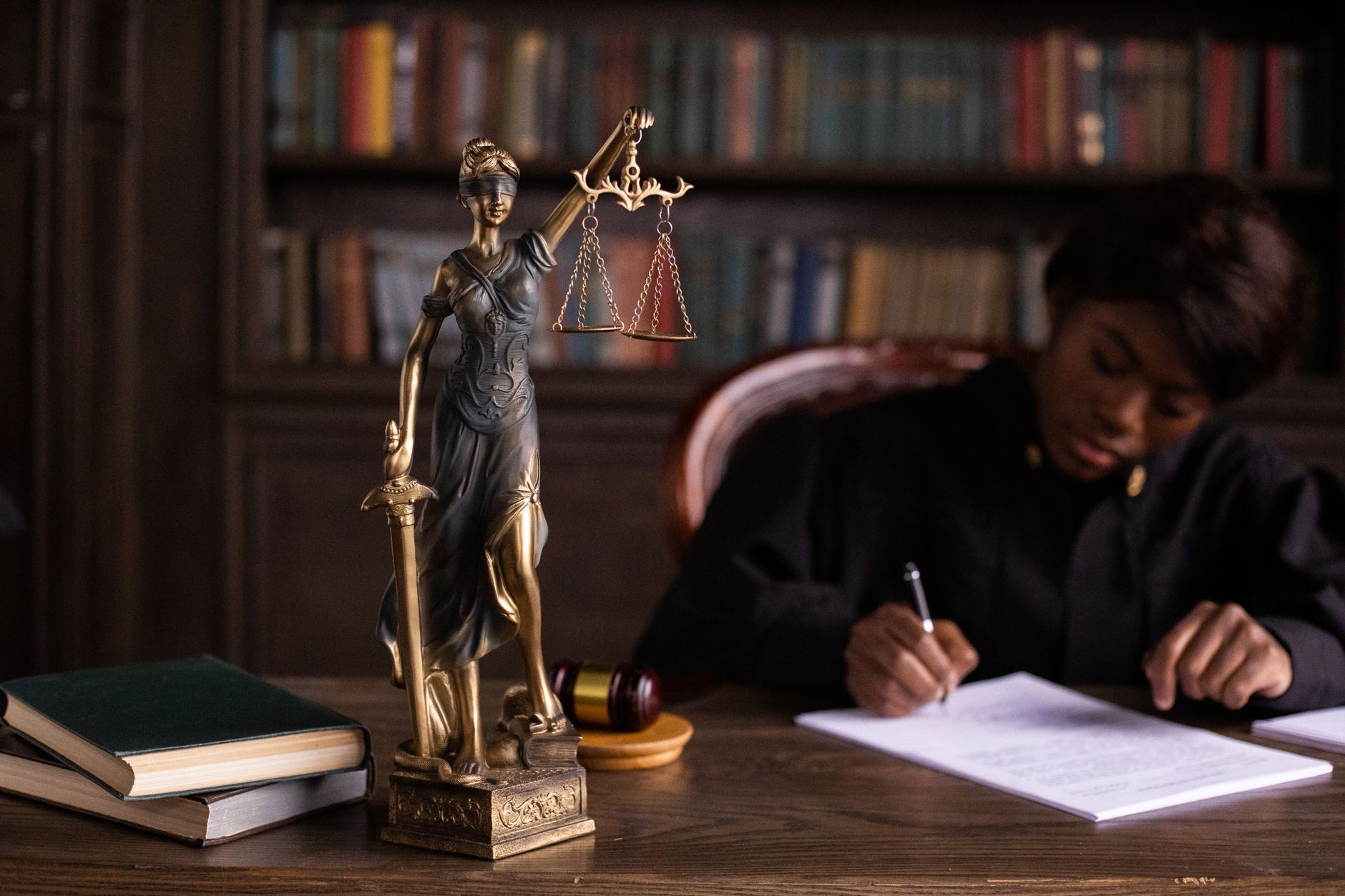 Juiz analisando documentos ao lado da estátua da Justiça em escritório com livros de direito