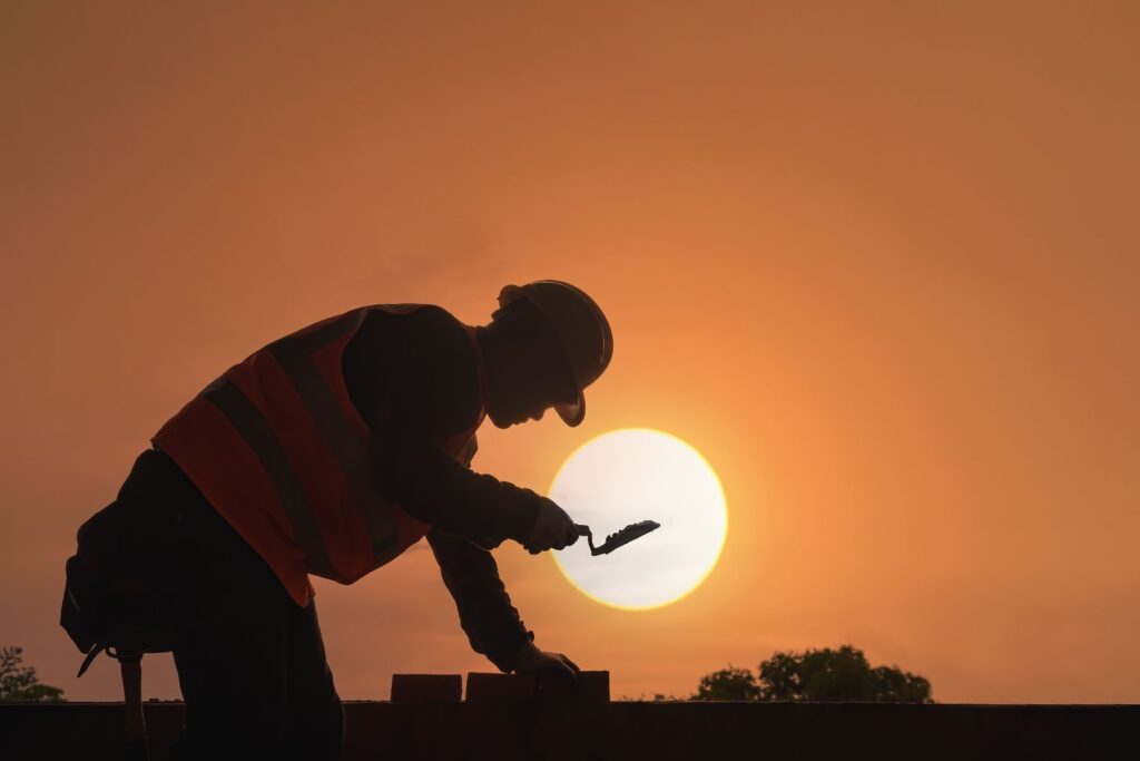Trabalhador da construção civil em silhueta contra o sol forte ao entardecer