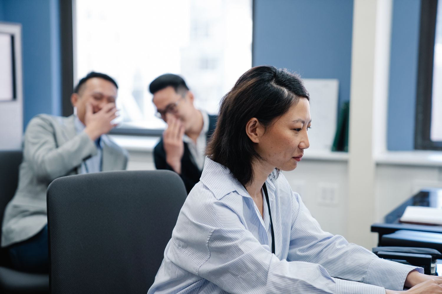Funcionária concentrada no trabalho enquanto colegas conversam e fofocam ao fundo no ambiente de escritório