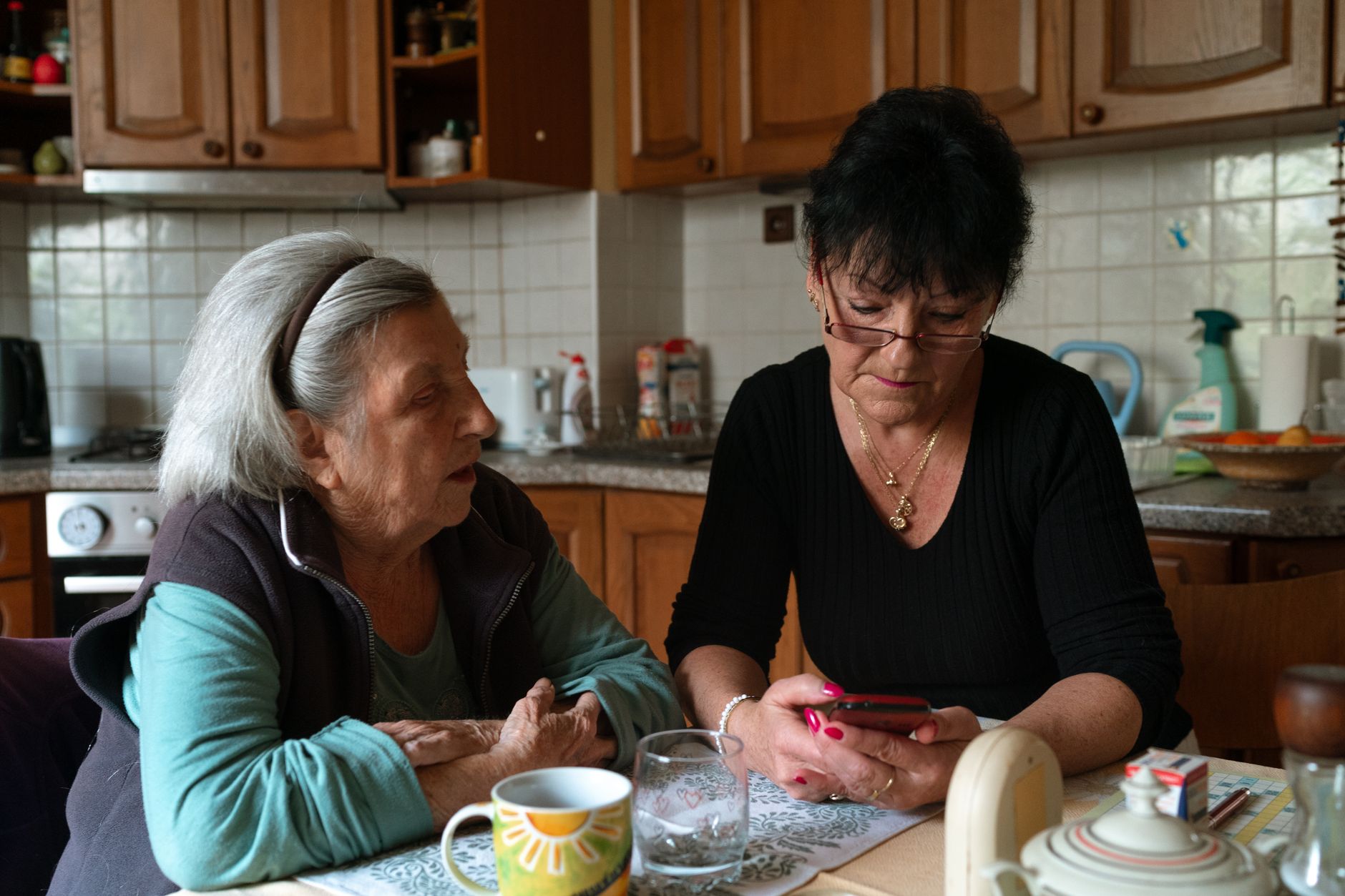 Cuidadora e idosa conversam na cozinha de casa