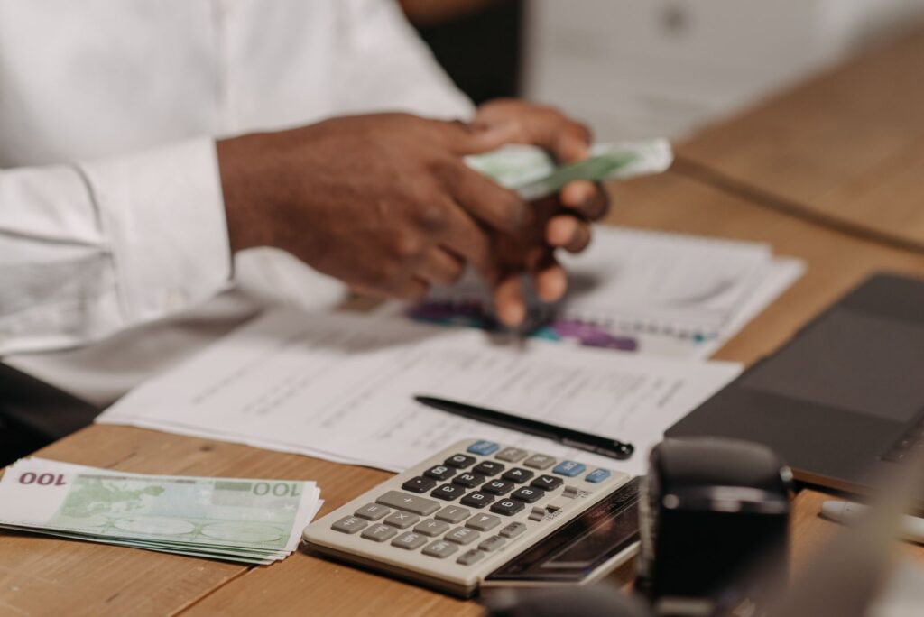 Mãos utilizam calculadora sobre mesa com documentos e dinheiro