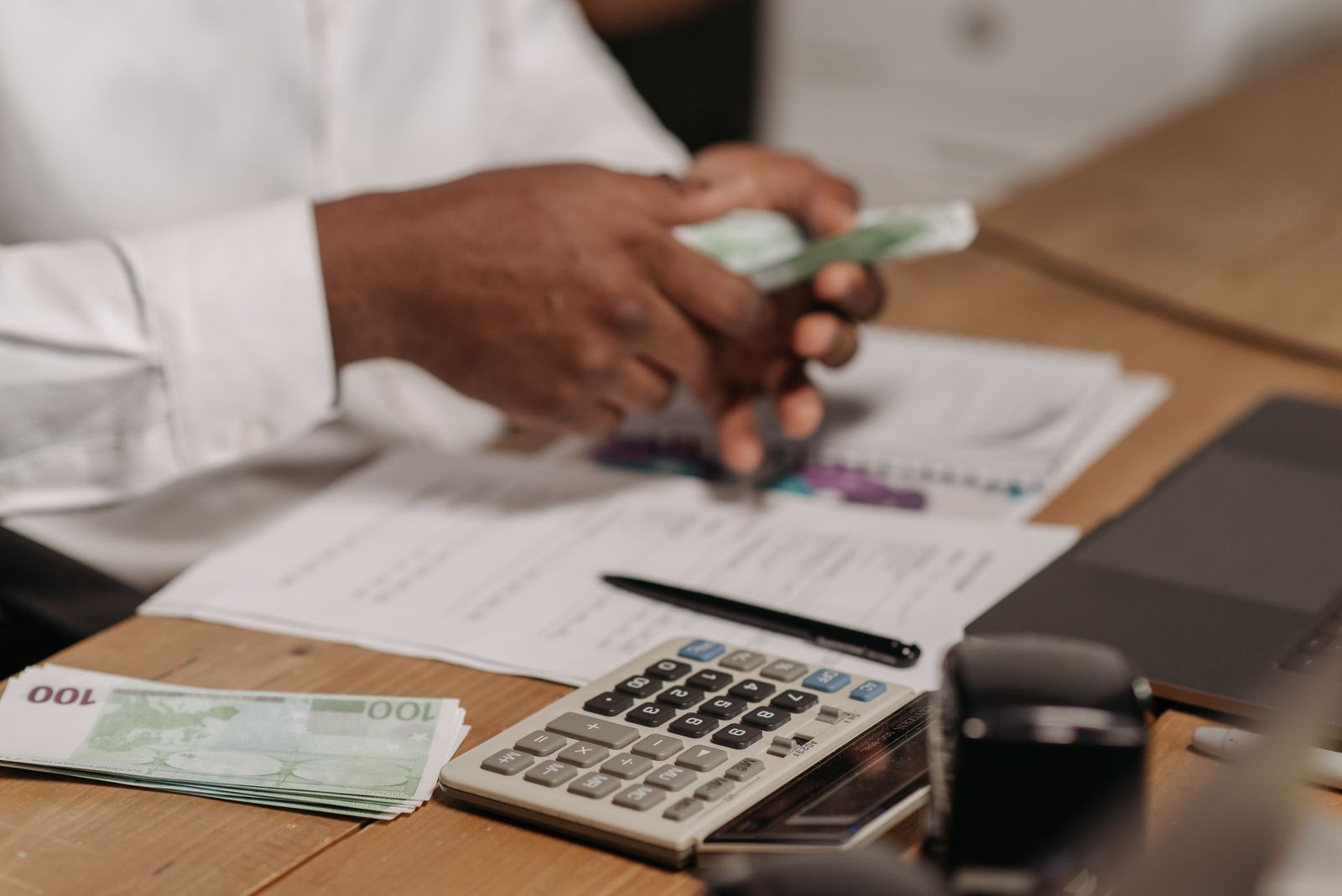 Mãos utilizam calculadora sobre mesa com documentos e dinheiro