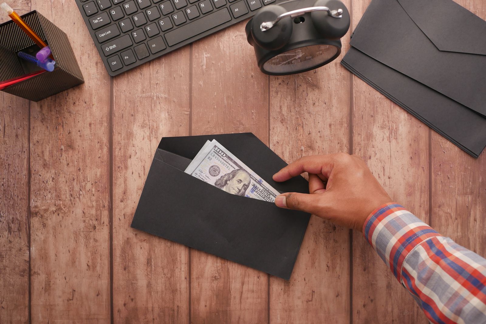 Mão entregando dinheiro dentro de envelope sobre a mesa