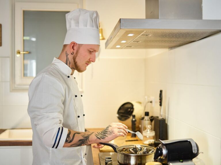 Cozinheiro tatuado de uniforme branco trabalhando em cozinha