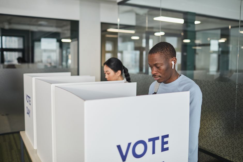 Duas pessoas votando em cabines de votação em local fechado