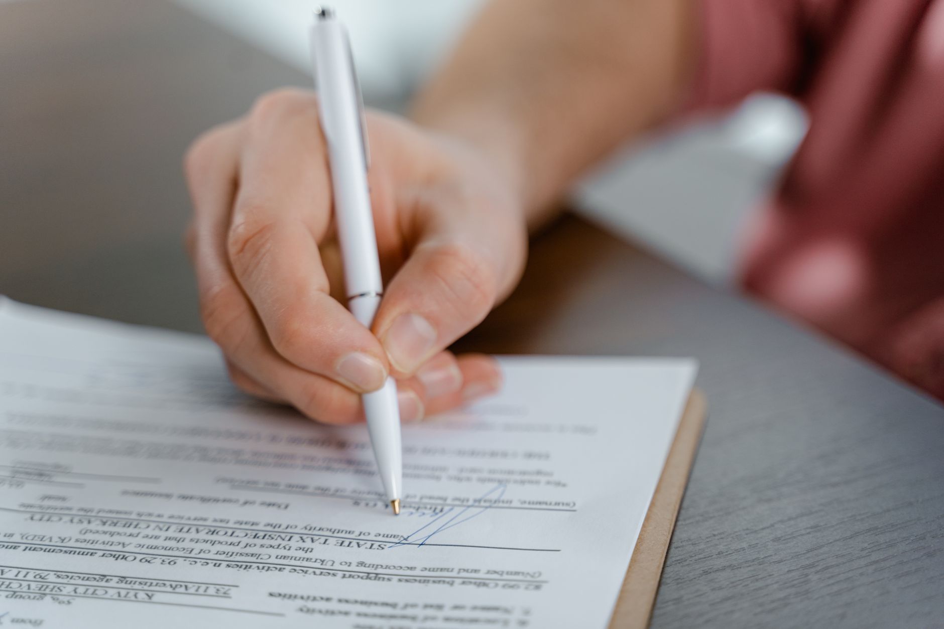 Mão assinando contrato de trabalho sobre mesa de escritório