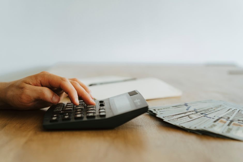 Mão usando calculadora sobre mesa para calcular o salário-hora