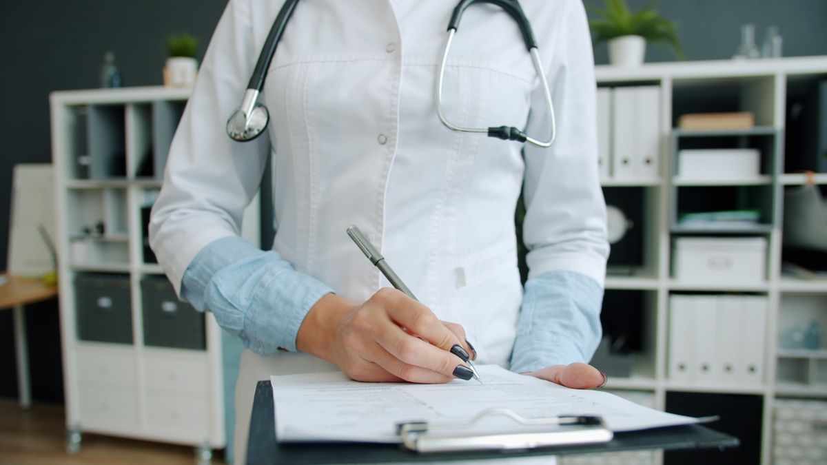 Médica de jaleco escrevendo anotações em prancheta durante consulta