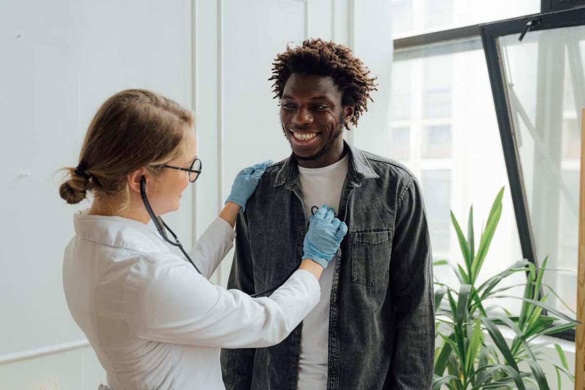 Médico de jaleco e estetoscópio atendendo paciente sorrindo em consultório