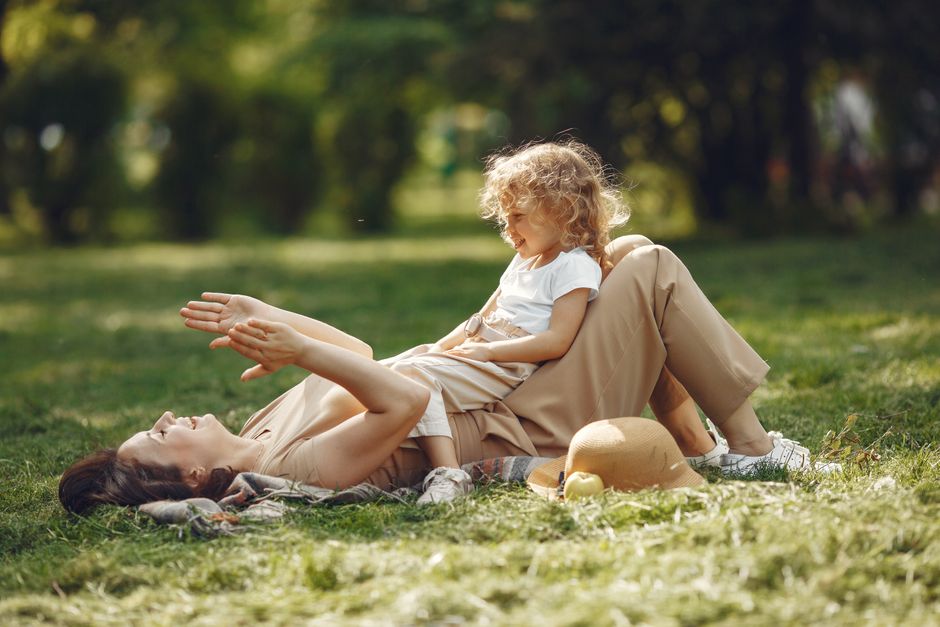 Mãe e filha brincando na grama em um parque ensolarado