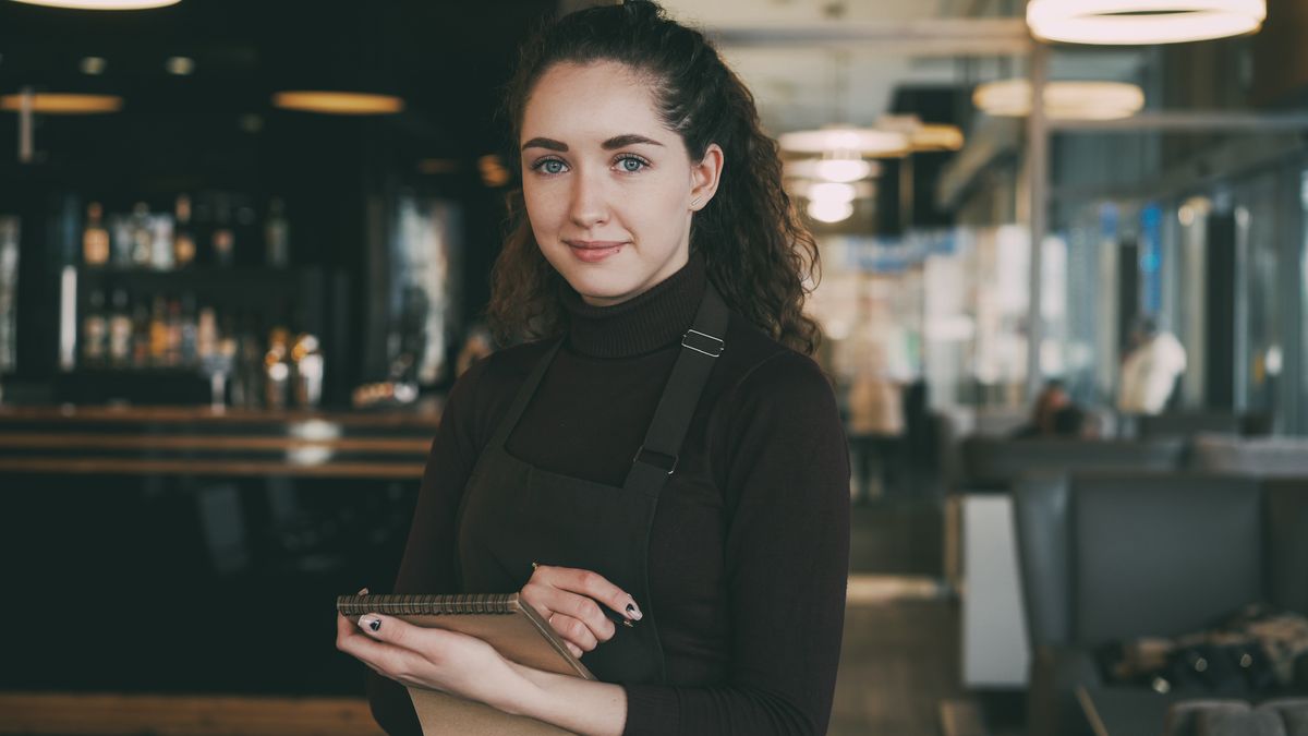 Garçonete sorridente com bloco de anotações em restaurante moderno