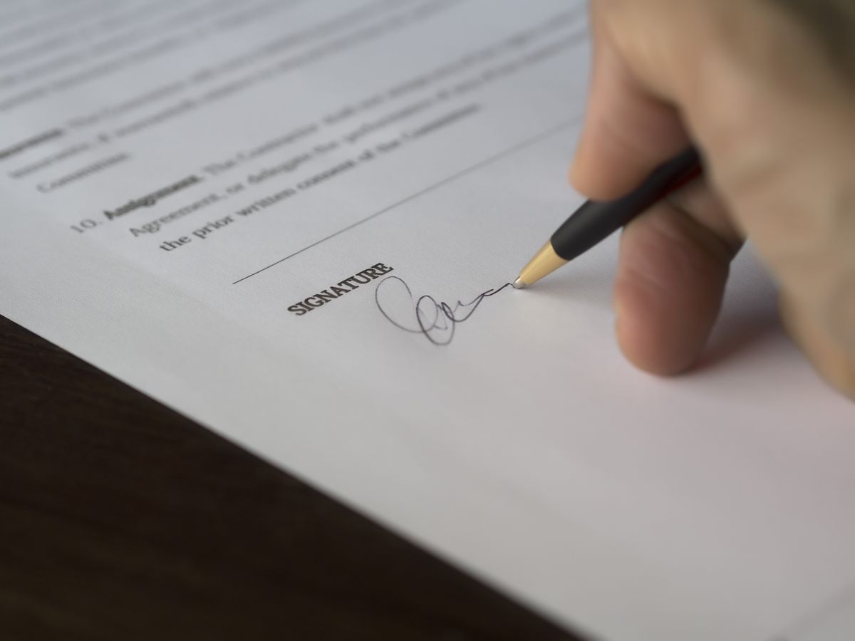 Mão assinando documento sobre mesa de escritório