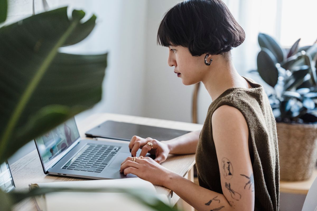 Mulher com tatuagens trabalhando sentada em frente a um notebook