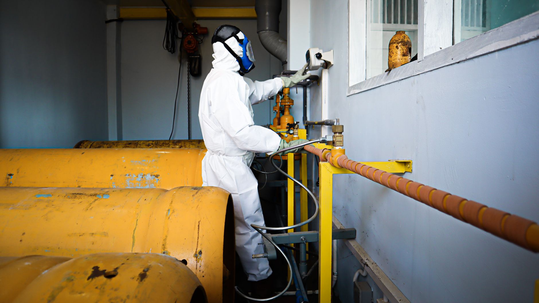 Trabalhador com macacão de proteção e máscara manuseando tubulações industriais