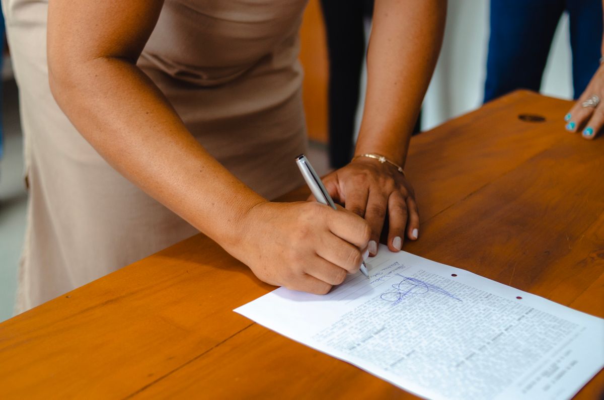Mulher assinando documento oficial sobre mesa de madeira