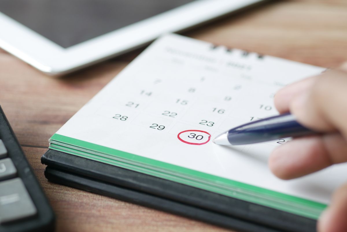Mão marcando uma data no calendário com caneta
