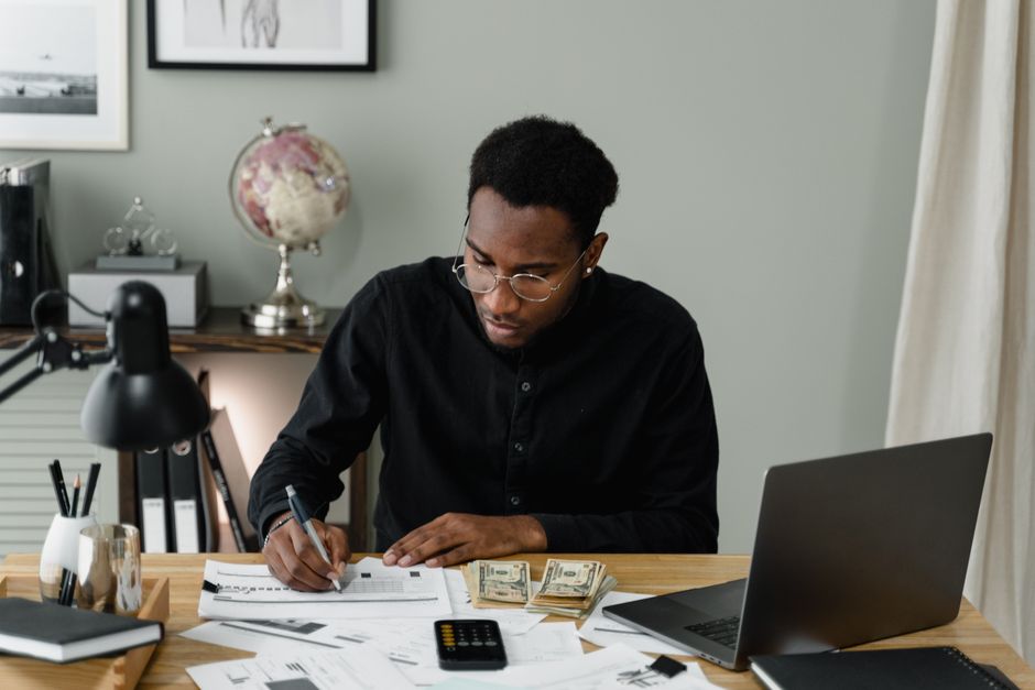 Homem calculando valores com documentos e notebook em uma mesa